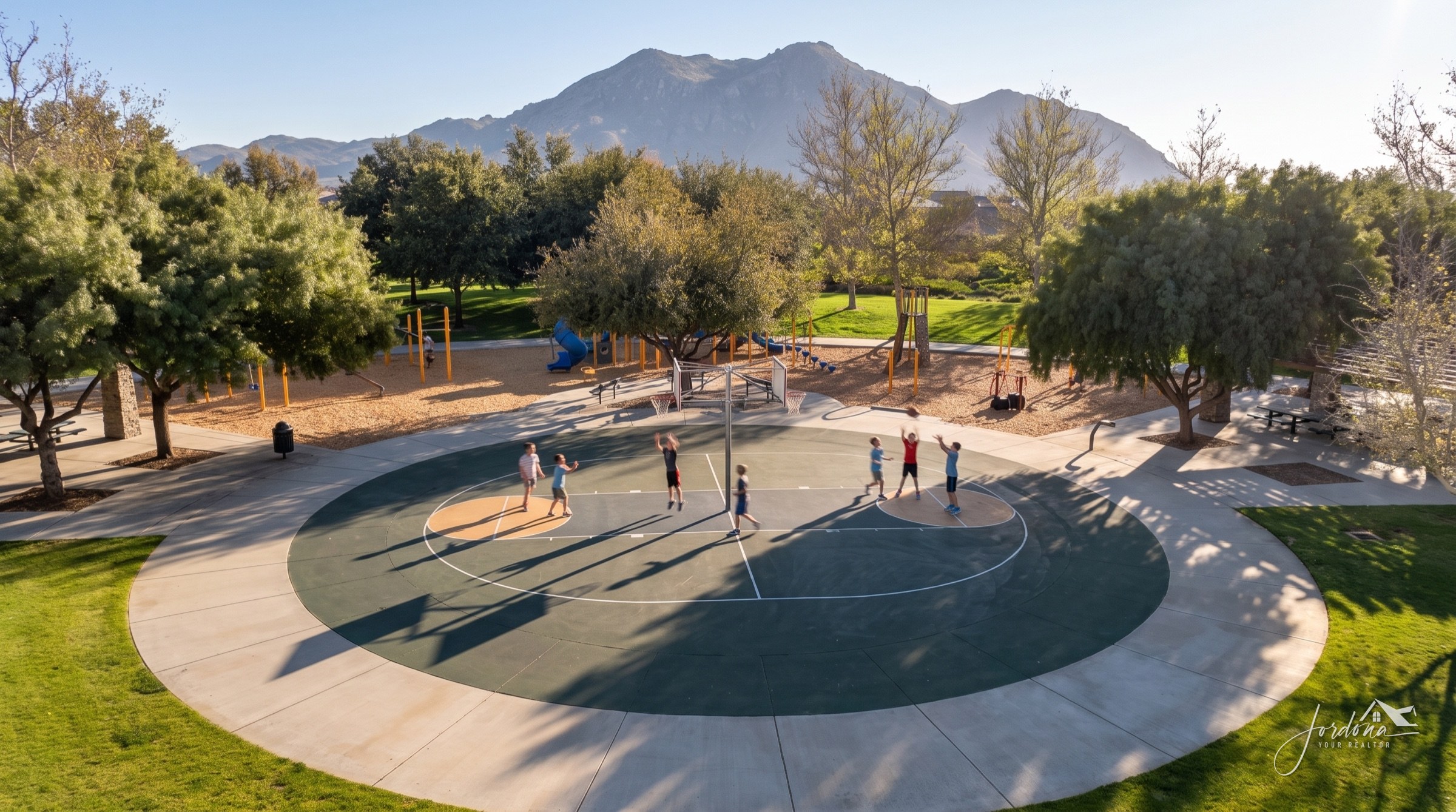 A pickup basketball game on the round court in a Heritage Lake park, with the playground and mountains behind