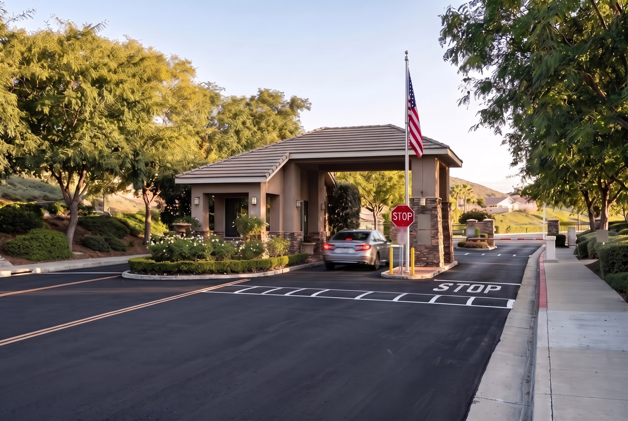 The gatehouse and entry drive at The Oasis, a gated 55+ community in Menifee, with the flag and stop line in afternoon light